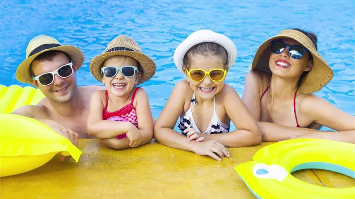 A happy family on a family vacation smiling in the pool wearing hats and sunglasses.