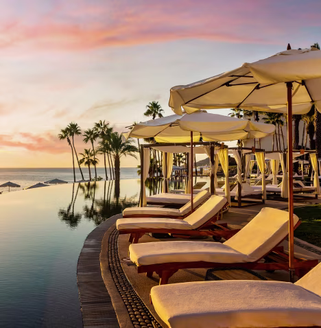 Sunset view of a serene infinity pool lined with empty lounge chairs and umbrellas