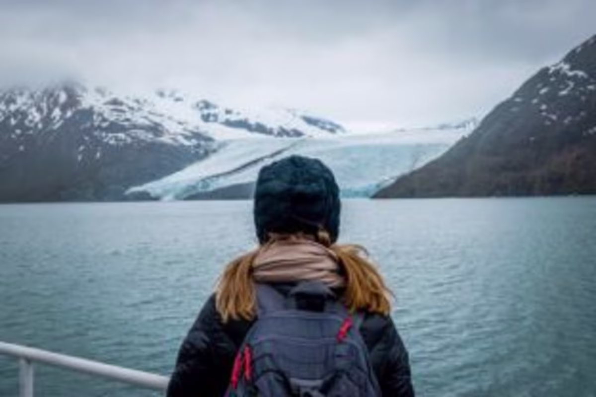 Woman gazing at water, snowcapped mountains, winter skies, Alaska cruise vacation.