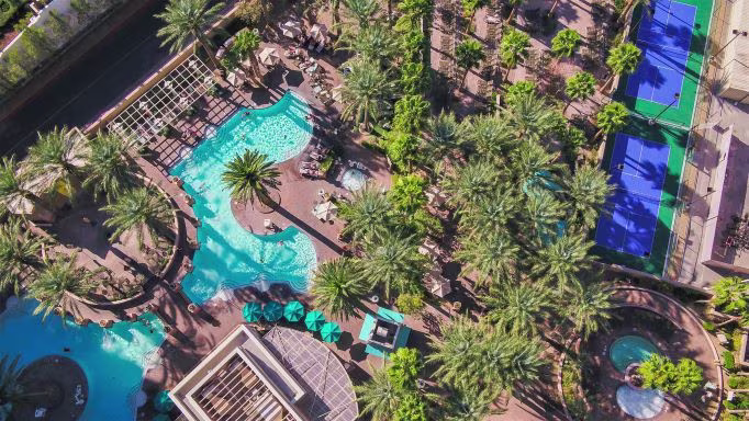Aerial view of the pool area at The Boulevard, a Hilton Grand Vacations Club, a resort in Las Vegas, with palm trees, pool chairs and tennis courts