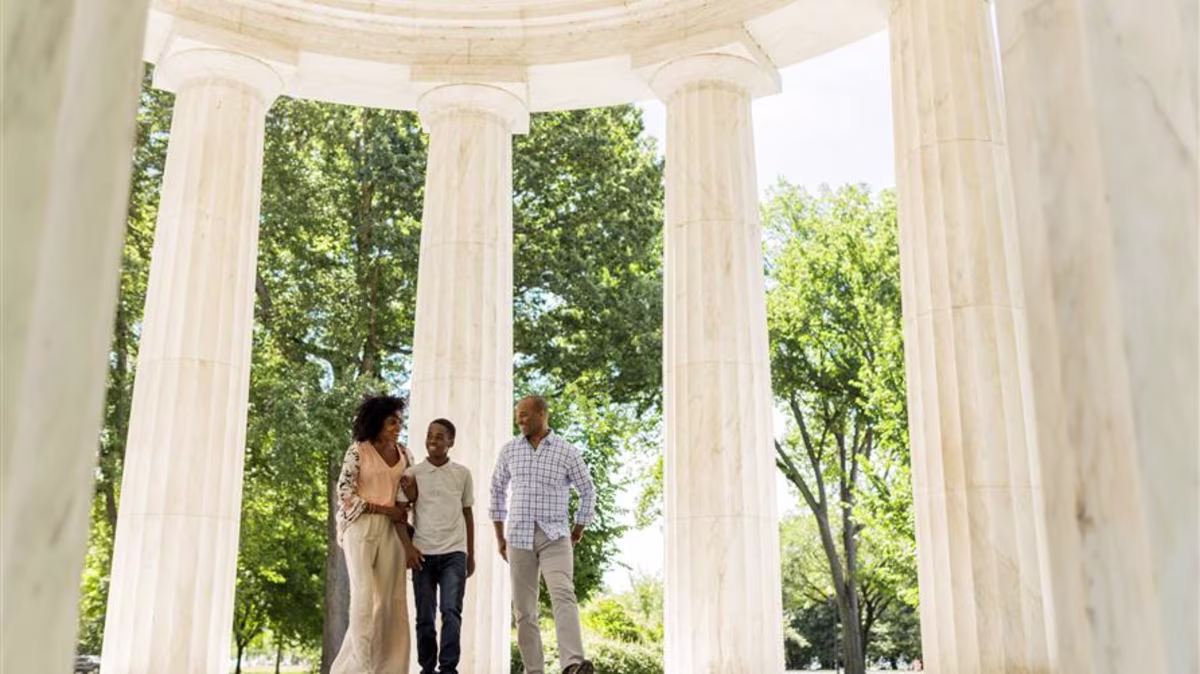 A family of three on vacation in Washington, D.C., posing in front of marble columns.