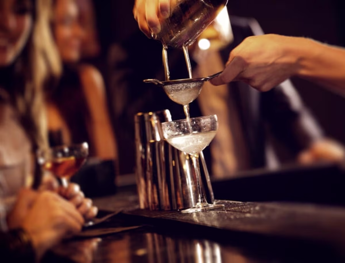 Bartender hand mixing cocktails at a bar.
