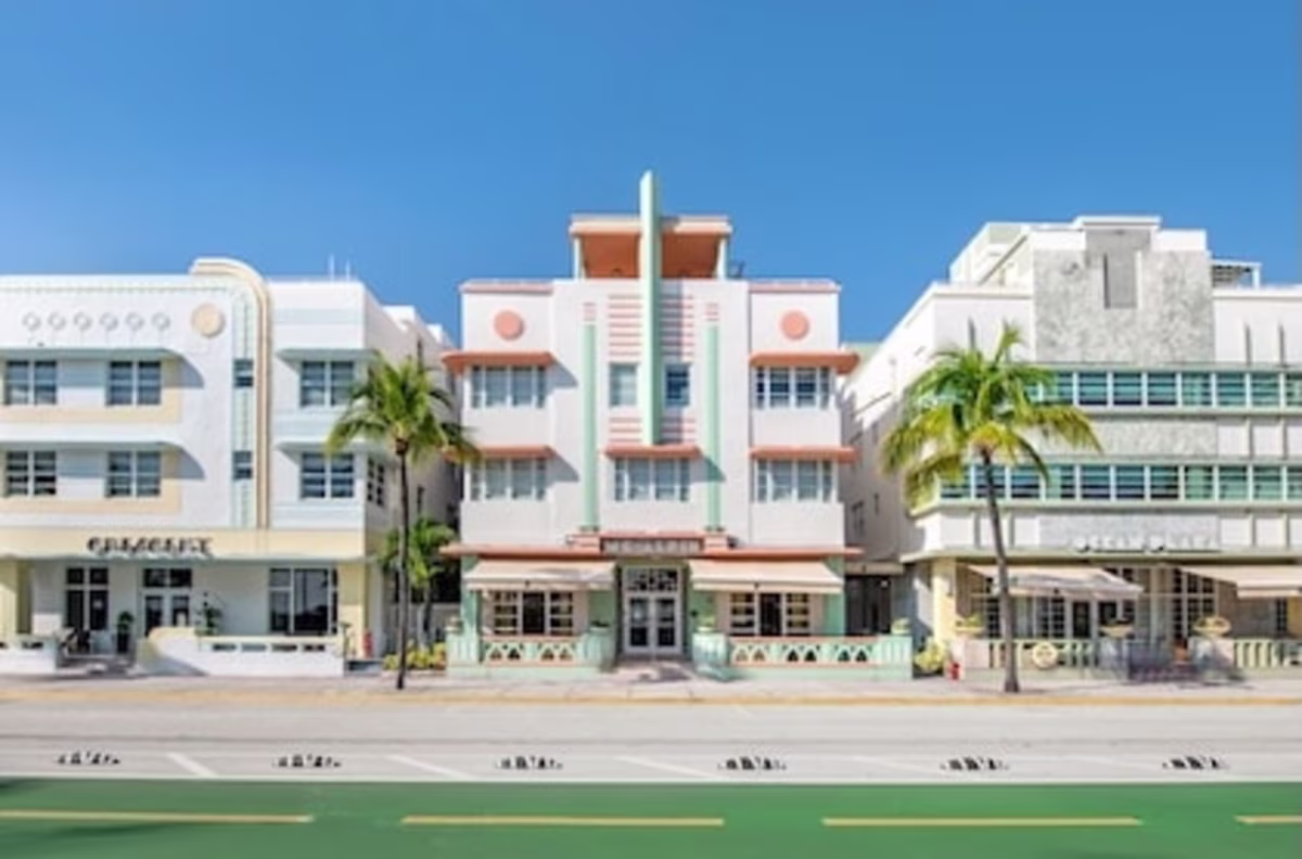Daytime street view of three pastel-colored art deco-style buildings on Collins Avenue in Miami, featuring McAlpin Ocean Plaza, a Hilton Grand Vacations Resort.