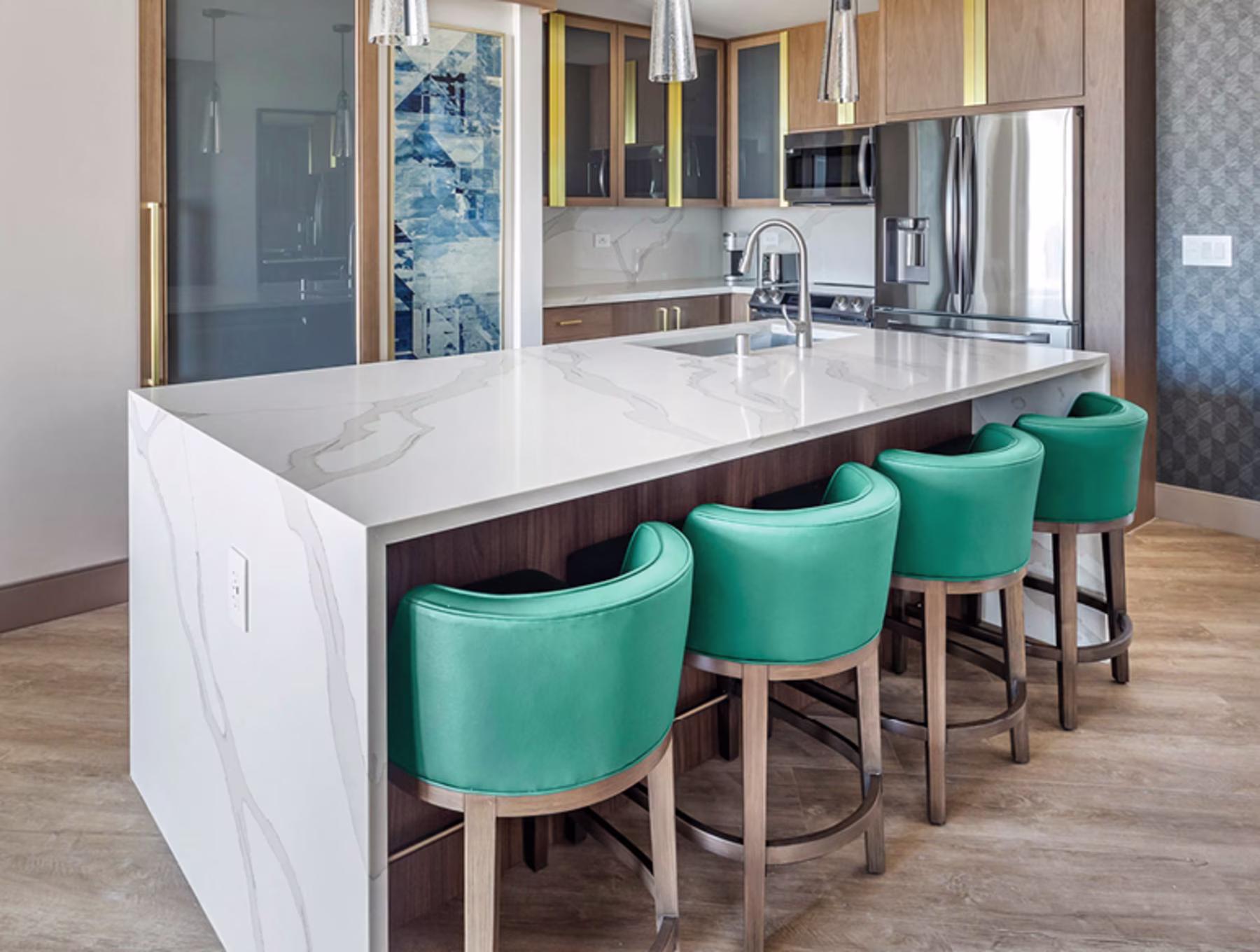 Modern kitchen with a large white marble island, surrounded by four teal leather chairs. Stainless steel appliances add a sleek, contemporary touch.