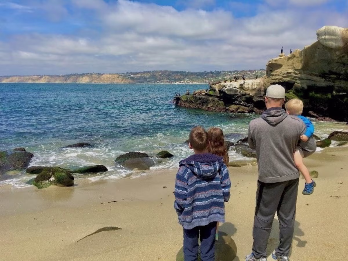 Father and kids looking out to the Pacific Ocean in a San Diego beach.