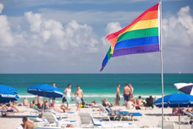 Pride flag on Miami Beach, beachgoers in the distance. 
