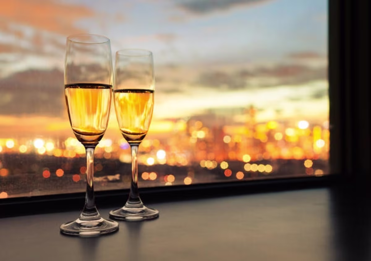 Two glasses of wine on a window ledge with city lights in the distance.