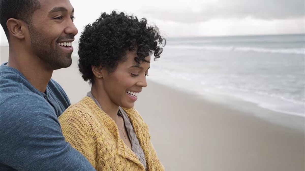 Couple holding each other on the beach staring out at the ocean hopefully.