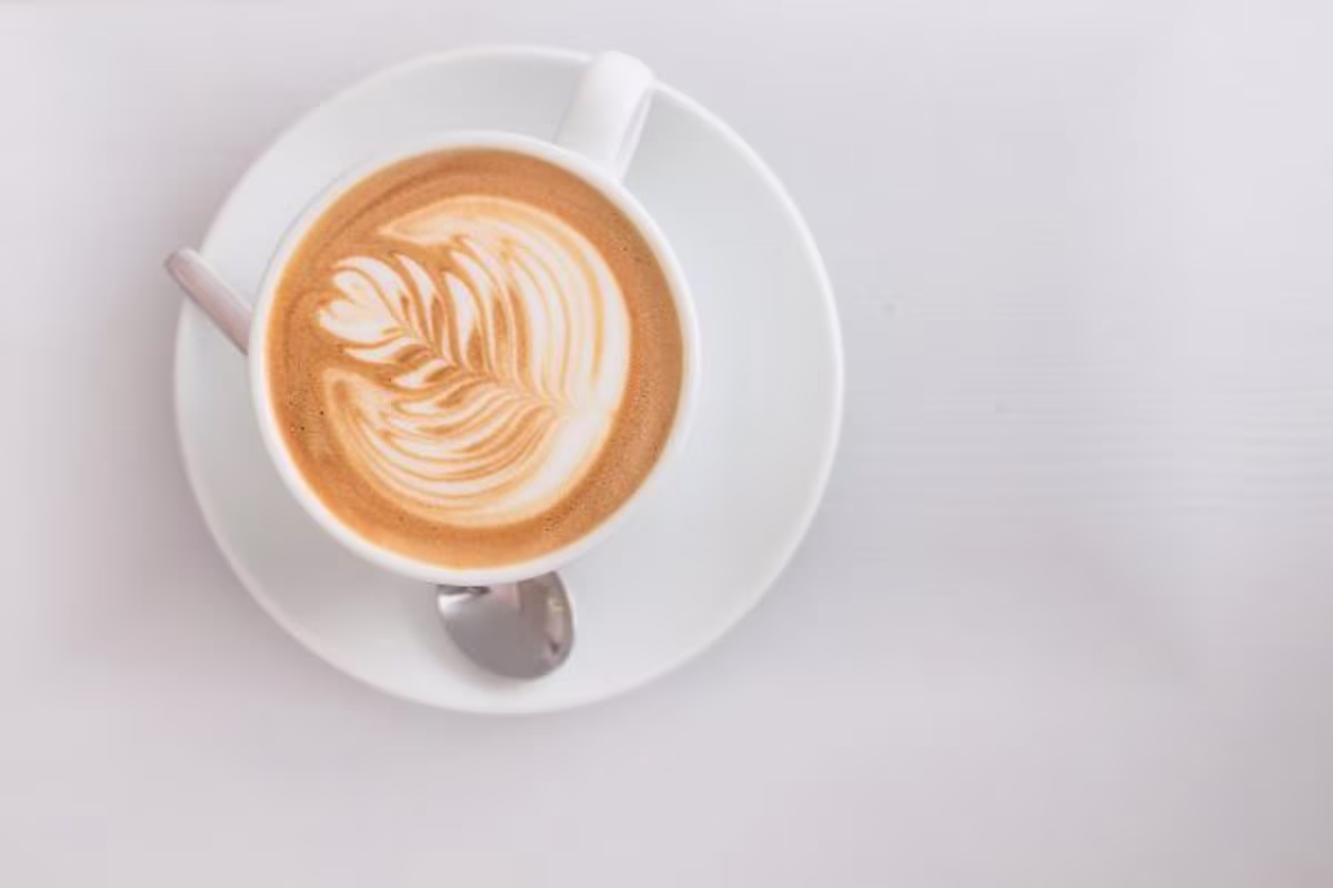 Overhead shot of coffee with coffee art on white table.