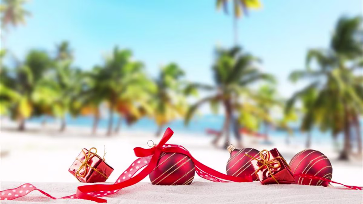 Christmas ornaments laying on the beach with palm trees in the background.