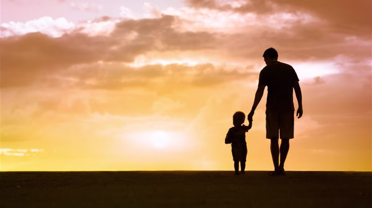 Silhouette of a father and young child holding hands and walking into the sunset.